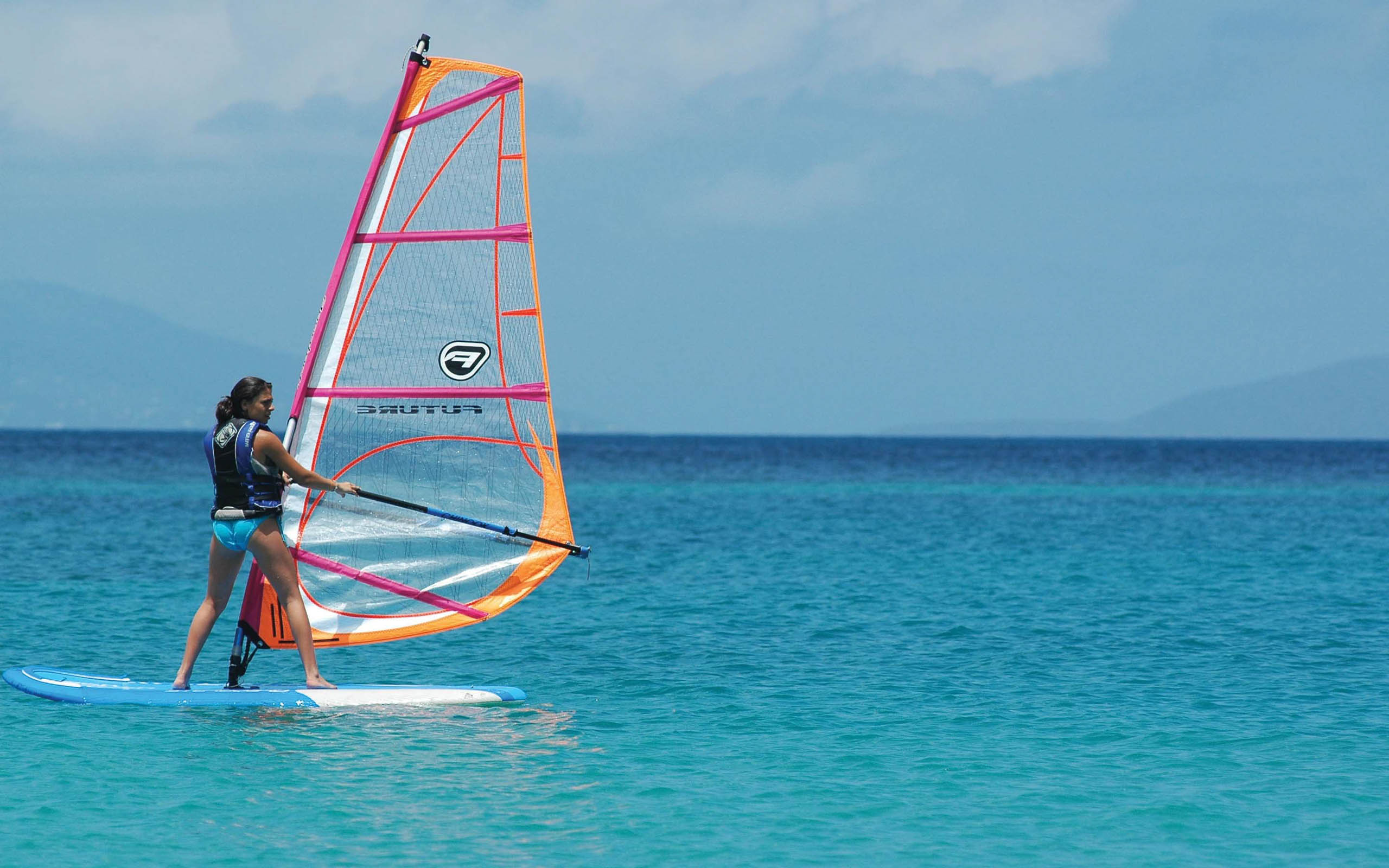 A woman is standing on a windsurf board in the ocean.