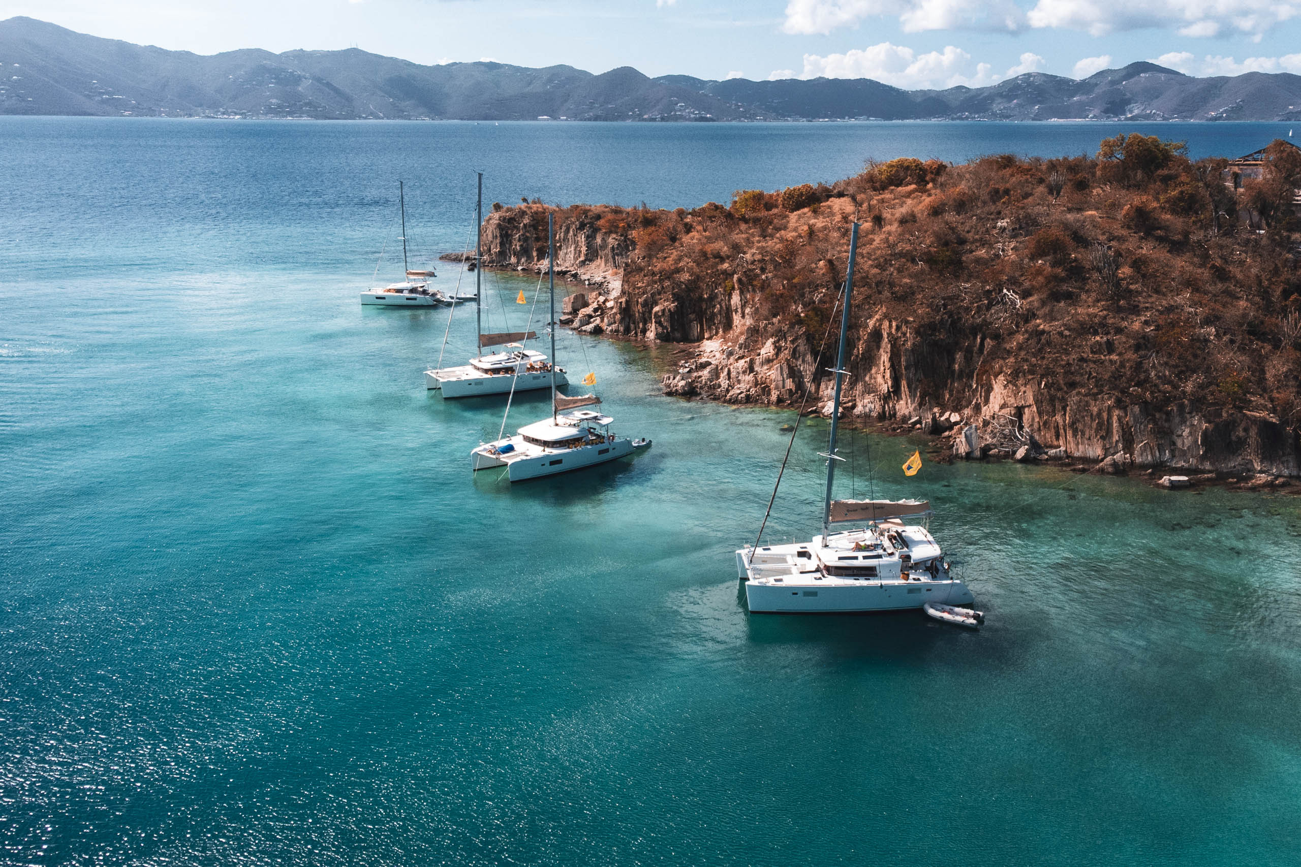 A group of sailboats docked near a rocky shore.