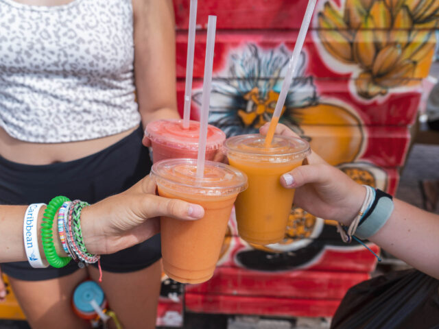 A group of people holding drinks in front of a mural.