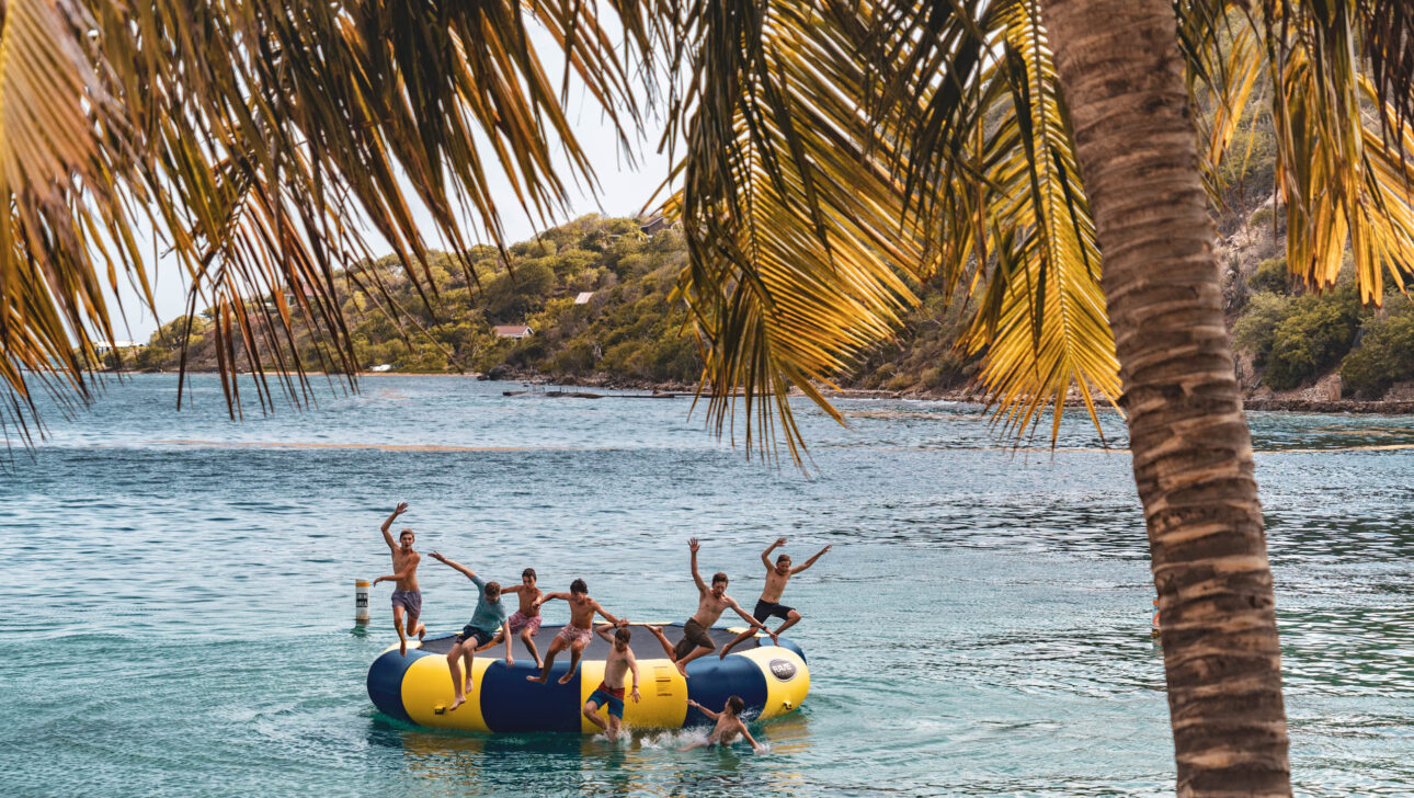 Campers jumping off on an inflatable raft in the water.
