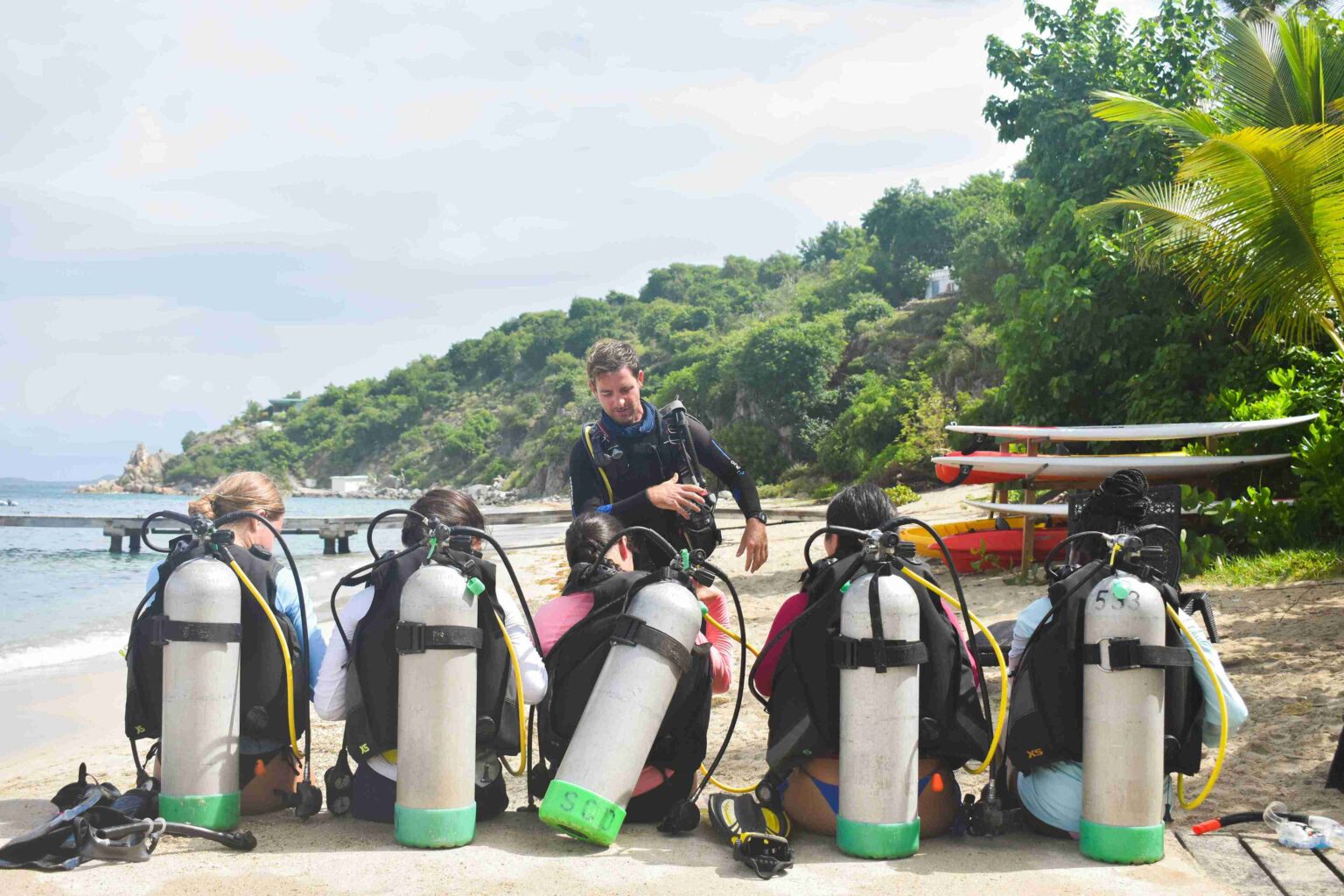 5 campers wearing scuba tanks and wetsuits, listening to their scuba instructor and learning about the basics of scuba diving.