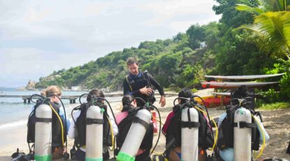 5 campers wearing scuba tanks and wetsuits, listening to their scuba instructor and learning about the basics of scuba diving.